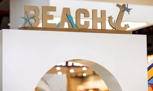 A shopping centre display featuring a white wooden arch with wooden letters and anchor, spelling BEACH for a summer display