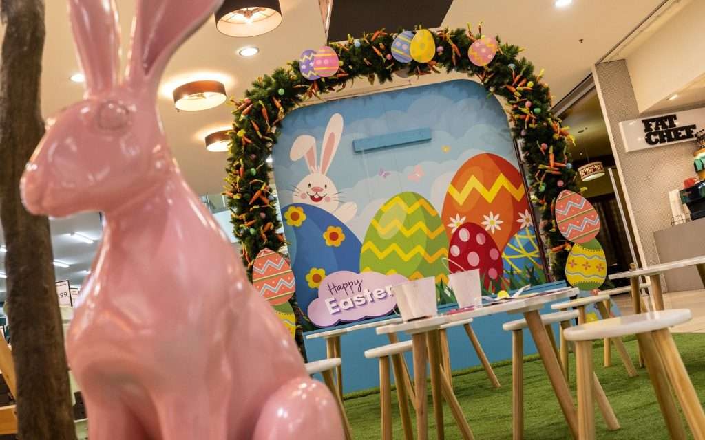 Easter bunny statue in pink in front of Easter seat with artwork