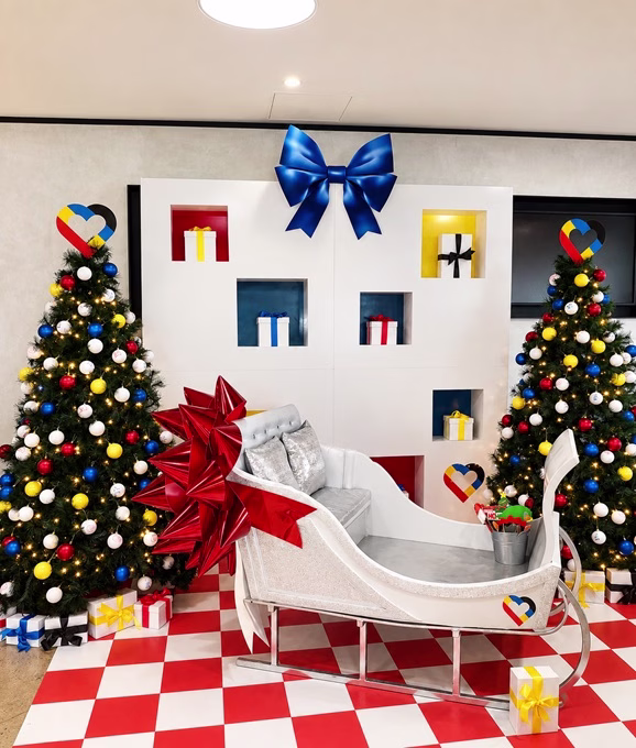 National Christmas campaign for BOQ. In the background, 2 Christmas trees covered in baubles in red, yellow, white and blue. A sleigh with huge red bow sits in the foreground.
