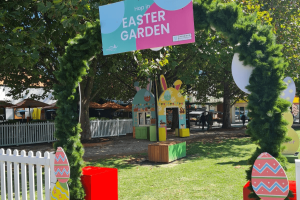 An archway reads Easter Garden. Through it we see a yellow bunny house on a lush lawn.