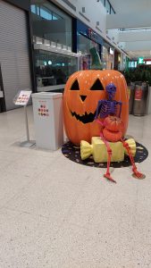 A skeleton sits on an oversized candy, leaning against a giant pumpkin