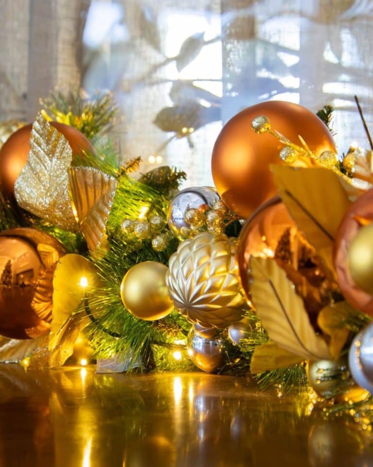 Close up of gold, copper Christmas baubles on a garland lying on a desk. The garland has warm white fairy lights