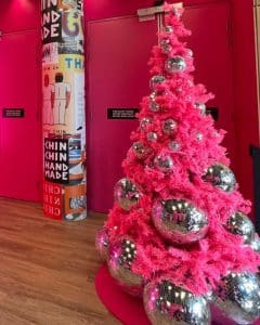 Pink Christmas tree in a pink room labelled Chin Chin. The tree is decorated with big dicso balls all over.