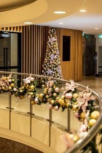 The Christmas tree and garlands are decorated in pink and gold with flowers and baubles.
