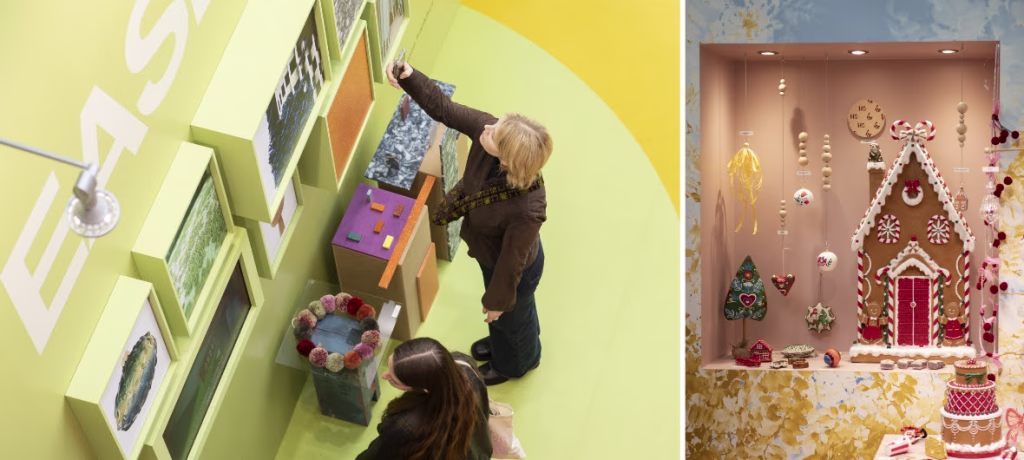 Two people are capturing Christmas decorative items on lime green wall shelves next to a festive holiday window display featuring a gingerbread house and Christmas ornaments