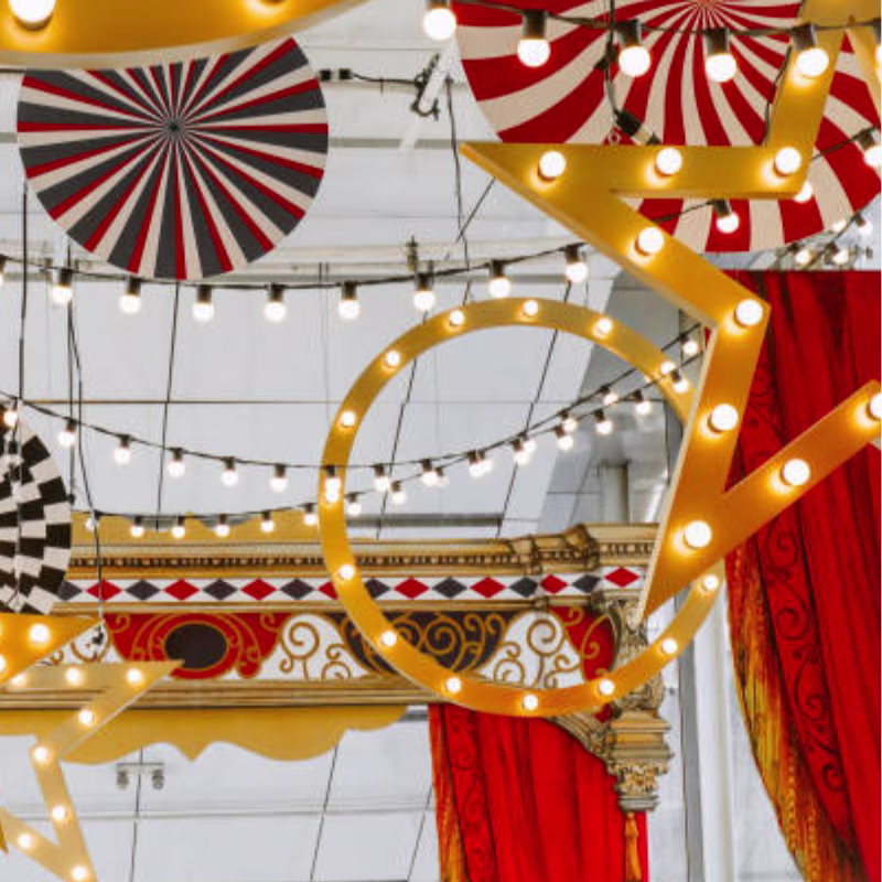 Hanging Vintage Circus themed shapes with large bulb lighting. Red, white and black swirls and stripes with red drapes.