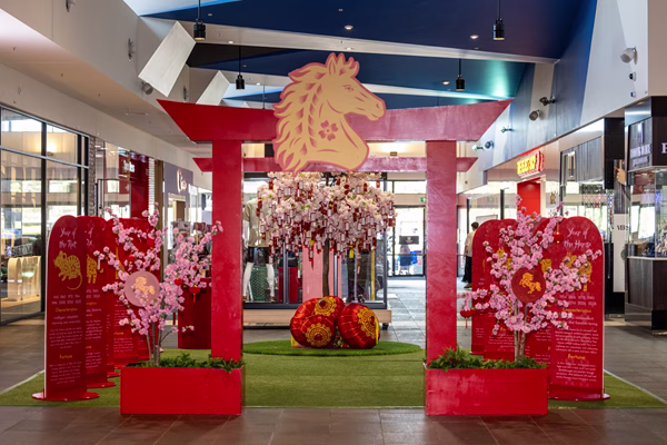 A striking shopping mall display featuring red torii gate with golden horse zodiac symbol, pink cherry blossom tree, decorative lanterns, and zodiac banners.