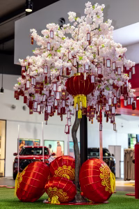 An artificial cherry blossom tree filled with Chinese red lanterns and red envelopes for wishes. Sitting in a commercial precinct at a shopping centre.