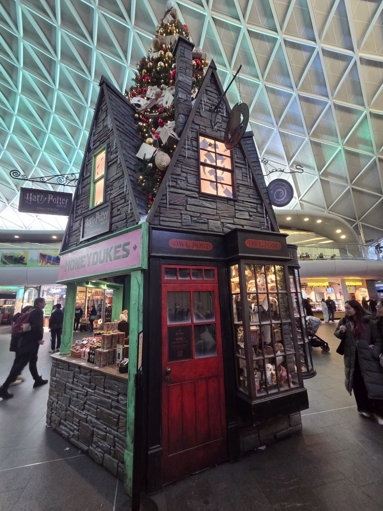 Large Christmast tree themed with a Honeyduke store and owl post office in the base from Harry Potter movies. Standing in Kings Cross station main casueway