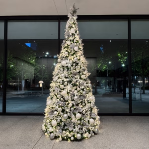 A white commercial Christmas tree display tree in white and silver baubles, winter floral picks and warm white fairy lights.