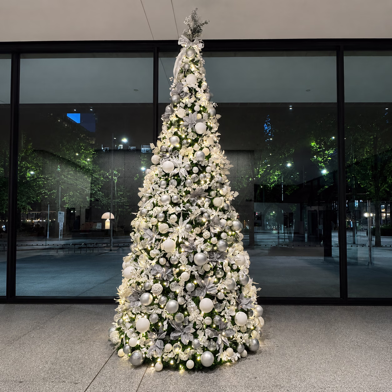 A white commercial Christmas tree display tree in white and silver baubles, winter floral picks and warm white fairy lights.