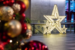Closeup of a Christmas tree with traditional red and gold baubles in front of a set of 3 LED warm white stars in gold.